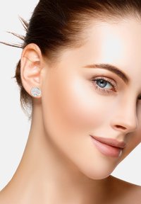 Silverfärgade studs i en cirkulär design med ett blommönster och stjärndetaljer, bärs av en modell med slät hy och slickat hår.