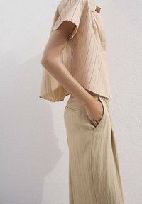 Top a maniche corte a righe gialle con una vestibilità rilassata, abbinato a pantaloni beige larghi con tasche laterali. Tessuto con una superficie liscia.