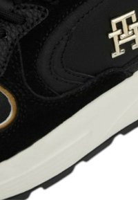 Sneaker nera realizzata in suede e mesh. Presenta un prominente logo dorato e una spessa suola intermedia bianca. Superficie texture con design a lacci.