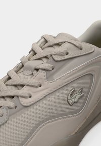 Baskets beige clair avec fermeture à lacets, matériaux en mesh et cuir, côtés texturés et petit logo argenté sur le côté.