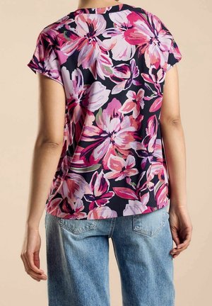 Květovaný top s krátkými rukávy v námořnické modři, zdobený velkými růžovými a fialovými květinami. Pohodlný střih s lehkou, splývavou látkou, doplněný světle modrými džínami.