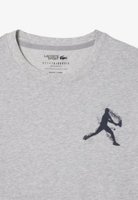 Camiseta de algodón gris con una silueta en color marino de un jugador de tenis en acción. Cuello redondo y marca impresa en el interior del cuello.