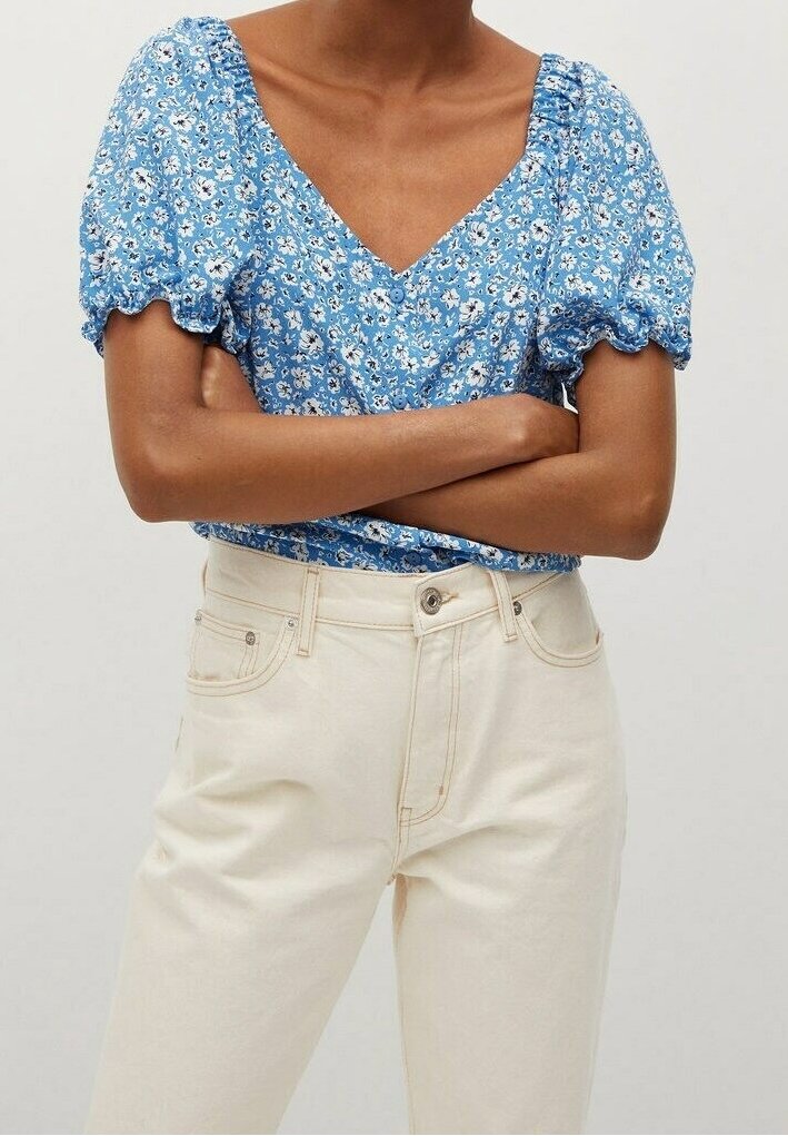 Haut à manches bouffantes à imprimé floral bleu avec un col en V et des détails froncés. Associé à un jean en denim crème taille haute.