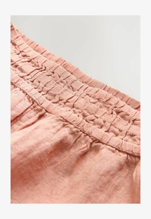 Cintura elastica di un rosa chiaro con texture arricciata. Il tessuto appare morbido e leggermente spiegazzato, indicando uno stile informale e traspirante.