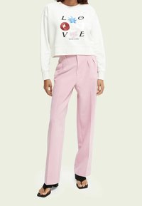 Sudadera blanca recortada con gráfico juguetón de "AMOR"; pantalones de tiro alto rosa con pliegues; sandalias negras de dedo al aire.