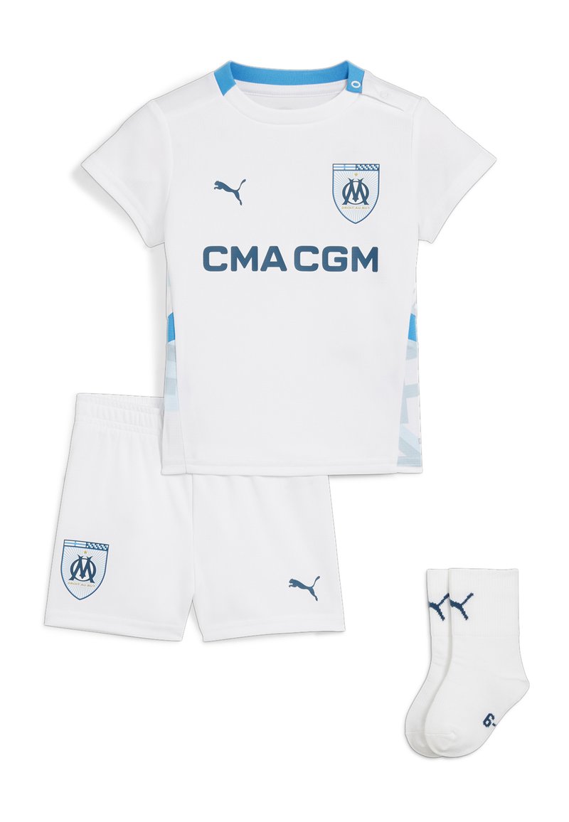 El conjunto de deportes juvenil blanco incluye una camiseta de manga corta, pantalones cortos y calcetas. Presenta acentos azules, logotipos y una cinturilla elástica.