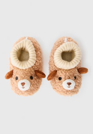 Chaussons pour bébé doux et beiges avec des visages d'ours, des oreilles brunes et des poignets côtelés blancs sur un fond clair.