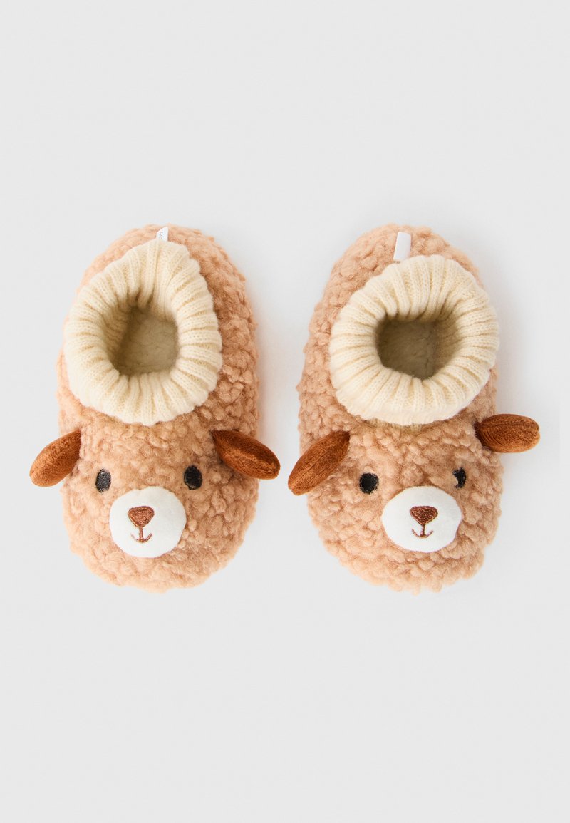 Myke, beige babysokker med bjørneansikter, brune ører og hvite ribbede mansjetter på en enkel lys bakgrunn.