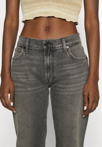 Jeans in denim grigio con vita alta, design a cinque tasche e una texture leggermente sbiadita. Presentano una chiusura con bottone e zip.