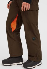Bruna vattentäta byxor med en orange mesh-foder har dragkedjeöppningar, cargofickor och en svart logotypficka på sidan. Svarta skor med texturerade sulor.