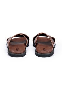 Sandali in pelle marrone con cinturini incrociati, suola piatta in gomma nera, texture liscia e design minimalista. Adatti per un abbigliamento casual.