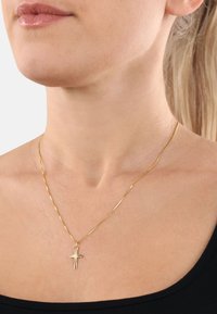Goldene Halskette mit einem Kreuzanhänger, ausgestattet mit einer gedrehten Kette und glatter Textur, die auf einem nackten Hals vor einem schlichten Hintergrund zur Schau gestellt wird.