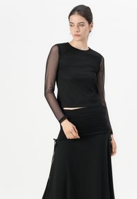 Black long-sleeve top with sheer mesh sleeves, paired with a ruched black skirt featuring drawstring accents at the waist.