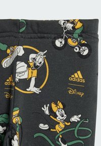 Leggings in cotone grigio con personaggi Disney in vivaci disegni a cartone gialli, verdi e bianchi, con il marchio Adidas stampato in fondo.