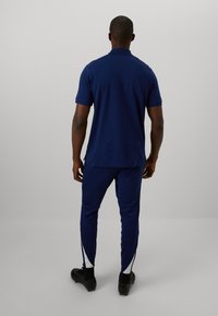 Marineblå polo t-shirt og matchende joggers, lavet af et glat stof. Joggers har sidelommer med lynlås, tætsiddende pasform og korte ærmer.