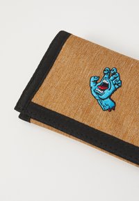 Brun stofflommebok med svart kant, med en blå brodert hånddesign. Overflaten har en teksturert, vevd utseende.