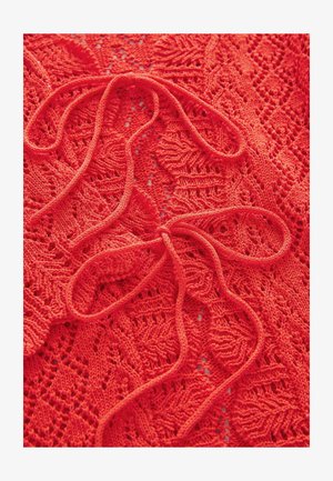 Punane kudumiskangas, millel on avatud pitsilised mustrid ja keskel eristuvad sidumisdetailid. Pehme tekstuur ja keerukad õmblusdetailid.