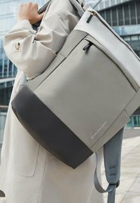 Zaino grigio e nero con finitura liscia, chiusura superiore con zip, spallacci imbottiti e dettagli del logo sul lato. Spallacci testurizzati per il massimo comfort.
