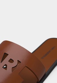 Καφέ δερμάτινο σανδάλι σαγιονάρας με μοτίβο κοψίματος στο λουράκι και μαύρη σόλα, εμφανίζεται πάνω σε λευκό φόντο.