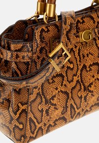 Bolso marrón de imitación piel de serpiente con herrajes dorados, que cuenta con dos asas y una forma estructurada. Destaca el logo de GUESS en la parte frontal.