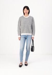 Fekete-fehér mintás pulóver, kerek nyakkal, világoskék skinny farmerral párosítva. Fekete kézitáska és díszített fekete lapos cipők.