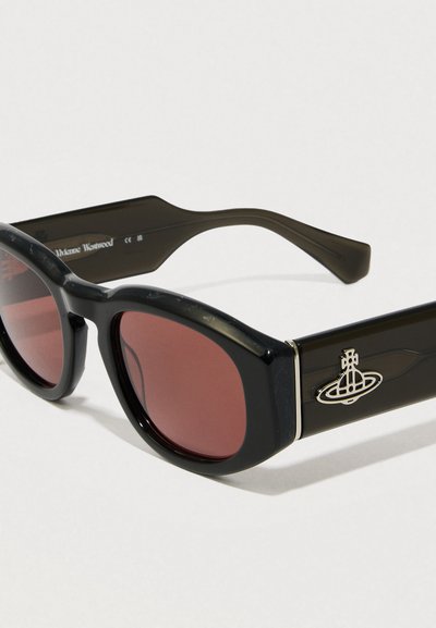 Fekete, oversized napszemüveg piros lencsékkel, fényes felülettel és ezüst logós díszítéssel a szárán. Egyedi szögletes keretforma.