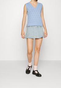 Ljusblå stickad ärmlös tröja med V-hals, i kombination med en denim mini kjol. Svarta lackläderskor med tjocka sulor och rosa strumpor.