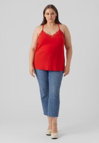 Red camisole with lace trim, paired with light blue cropped jeans. Model wears beige platform heels, standing against a plain background.
