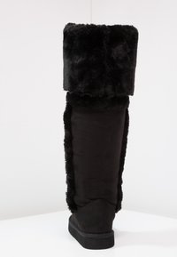 Svarta knähöga stövlar med en fake pälsfåll, mjuk textur, släta sidor och en platt gummisula, designade för värme och komfort.