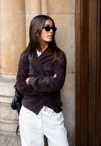 Mörkbrun, fluffig omslagsjumper, vita byxor, svart handväska och svarta solglasögon. Slät yta med avslappnad passform och asymmetrisk fåll.