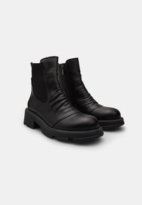 Botas de cuero negro hasta el tobillo con punta redonda, paneles laterales elásticos y parte superior texturizada. Presentan un tacón robusto y cierre de cremallera.