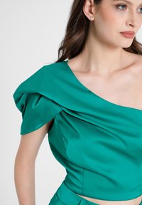 Türkisfarbenes Satin-Oberteil mit einseitigem Design, plissierten Details und glatter Textur. Mit kurzen, drapierten Ärmeln und kürzerer Länge.