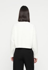 Weißer, verkürzter Pullover mit geripptem Saum und Bündchen, mit lockerer Passform und weicher Textur, kombiniert mit hochgeschnittenen schwarzen Hosen.