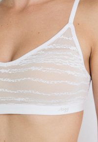 White bra made of mesh material with a wavy pattern, featuring thin straps and a branded elastic band at the bottom.