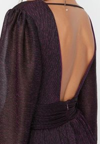 Tył głębokofioletowej sukienki z niskim dekoltem, marszczonym materiałem w talii oraz miękkimi, teksturowanymi długimi rękawami.