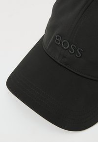 Cappello nero realizzato in tessuto morbido, con visiera curva e logo "BOSS" ricamato tono su tono sul davanti. Accentuato da dettagli di cucitura.