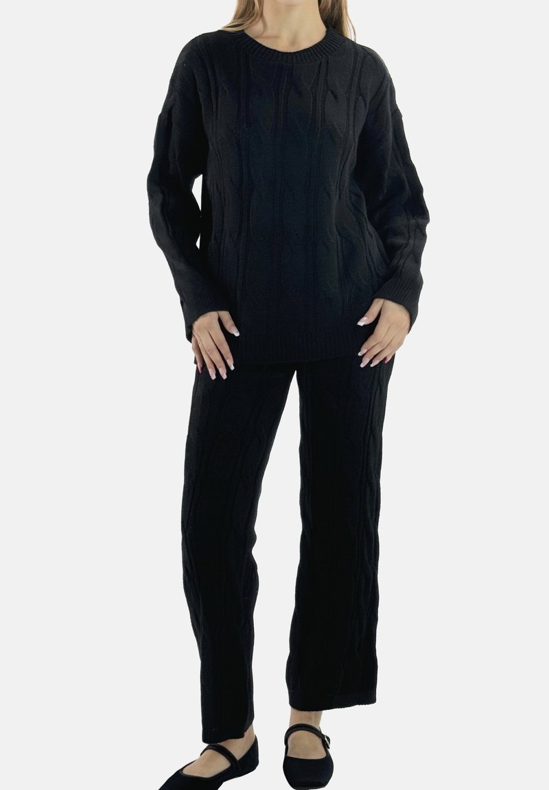 Sort strikket sweater og bukser med et tekstureret kabelmønster. Sweateren har rund hals, og sættet ledsages af sort fodtøj.