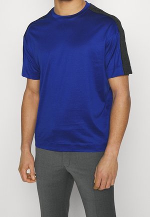 T-shirt bleu à manches courtes en tissu lisse avec un col rond et des accents texturés noirs sur les épaules. Coupe ajustée sans motifs.
