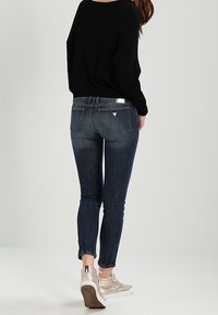 Dunkelblaue Skinny Jeans mit einer mittelhohen Taille, subtilen Ausbleichungen und einem Design für die Gesäßtasche. Kombiniert mit hellbeigen Sneakers.