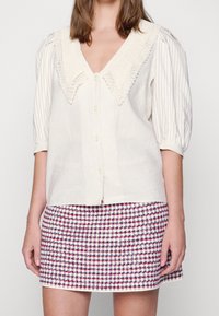 Krämfärgad randig blus med en stor stickad krage och korta puffärmar, tillsammans med en mini kjol i röd och vit hundtandsmönster.