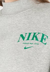 Grå höghalssweatshirt med grön text "NIKE Athletic dept. 1972" och liten Nike swoosh-logotyp på bröstet.