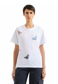 Hvid t-shirt med korte ærmer, prydet med farverige sommerfugldesigns i brun, pink, blå og sort. Glat stof med en afslappet pasform.