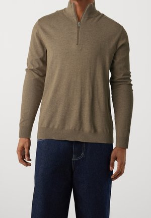 Maglione marrone con zip al collo realizzato in materiale morbido, caratterizzato da maniche lunghe, polsini a coste e un orlo aderente, abbinato a jeans blu scuri.