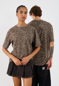 Ruskea leopardikuosisella t-paidalla, joka on valmistettu pehmeästä kankaasta, pyöreä pääntie, lyhyet hihat, yhdistetty mustiin denimpushoihin, joissa on puristetut reunat.