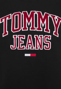 Černá mikina s velkým bílým a červeným vyšitým textem "TOMMY JEANS" a malou vyšitou červenou, bílou a modrou pruhovanou aplikací pod ním.