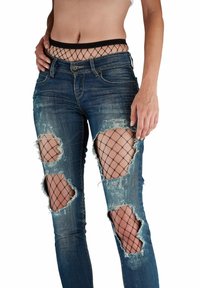Jean en denim bleu avec de multiples déchirures usées, révélant des couches de résille noires en dessous. Texture décolorée et coupe slim. Ceinture élastique noire.