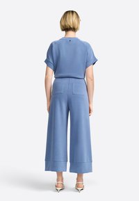 Lichtblauw tweedelig outfit met een losse top met opgerolde mouwen en wijde broekspijpen met twee achterzakken. Gladde stof textuur.