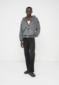 Hanorac gri cu fermoar, șnururi, buzunare în față și manșete nervurate; asortat cu blugi negri cu picioare largi și încălțăminte închisă la culoare.