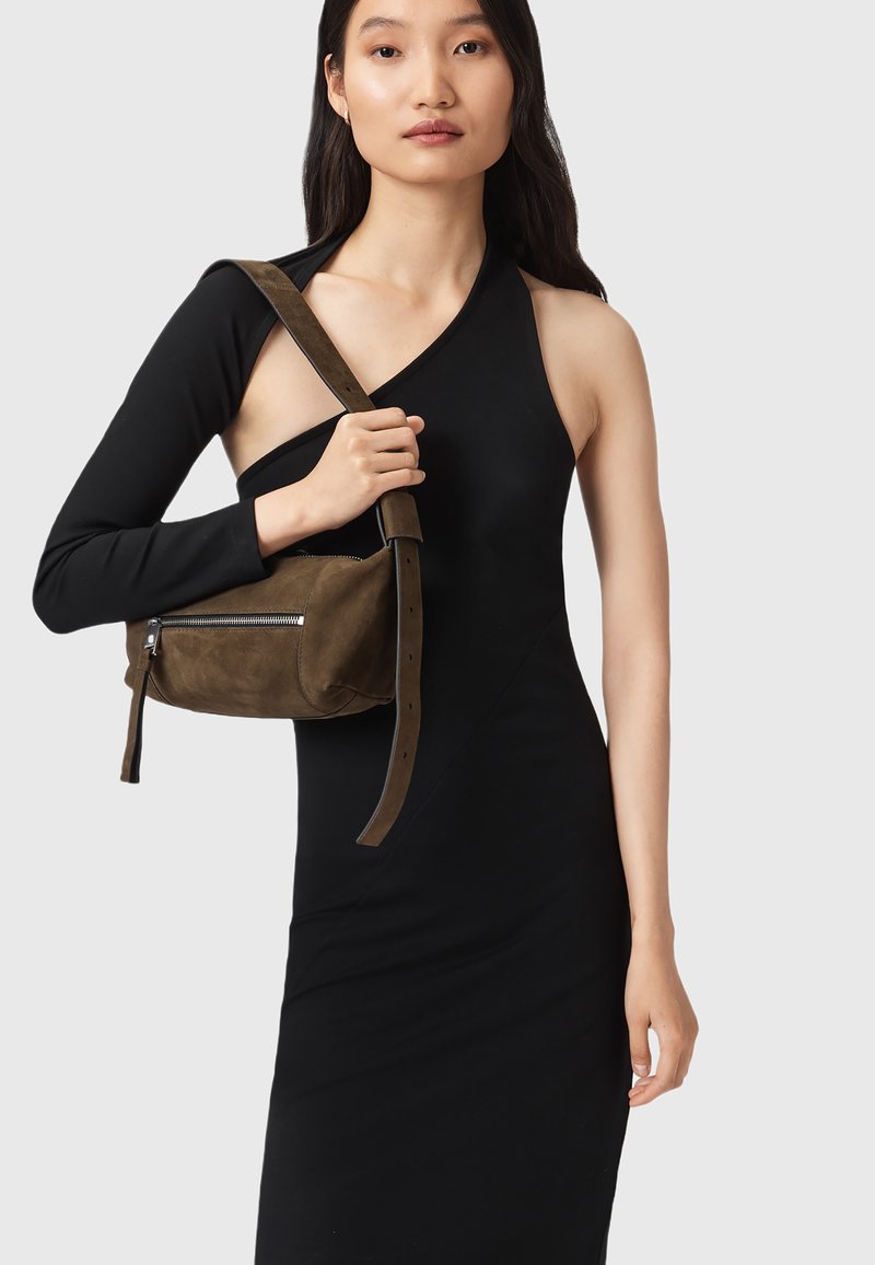 Vestido negro ajustado con un lado sin mangas, combinado con un pequeño bolso de hombro de ante marrón, que cuenta con una cremallera y una correa ajustable.