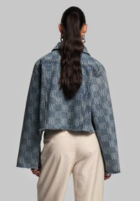 Jeansjacke mit einem gekürzten Design in hellblauem Farbton, komplettem Logo-Muster und ausgefranster Saumkante. Lange Ärmel mit breiten Manschetten.